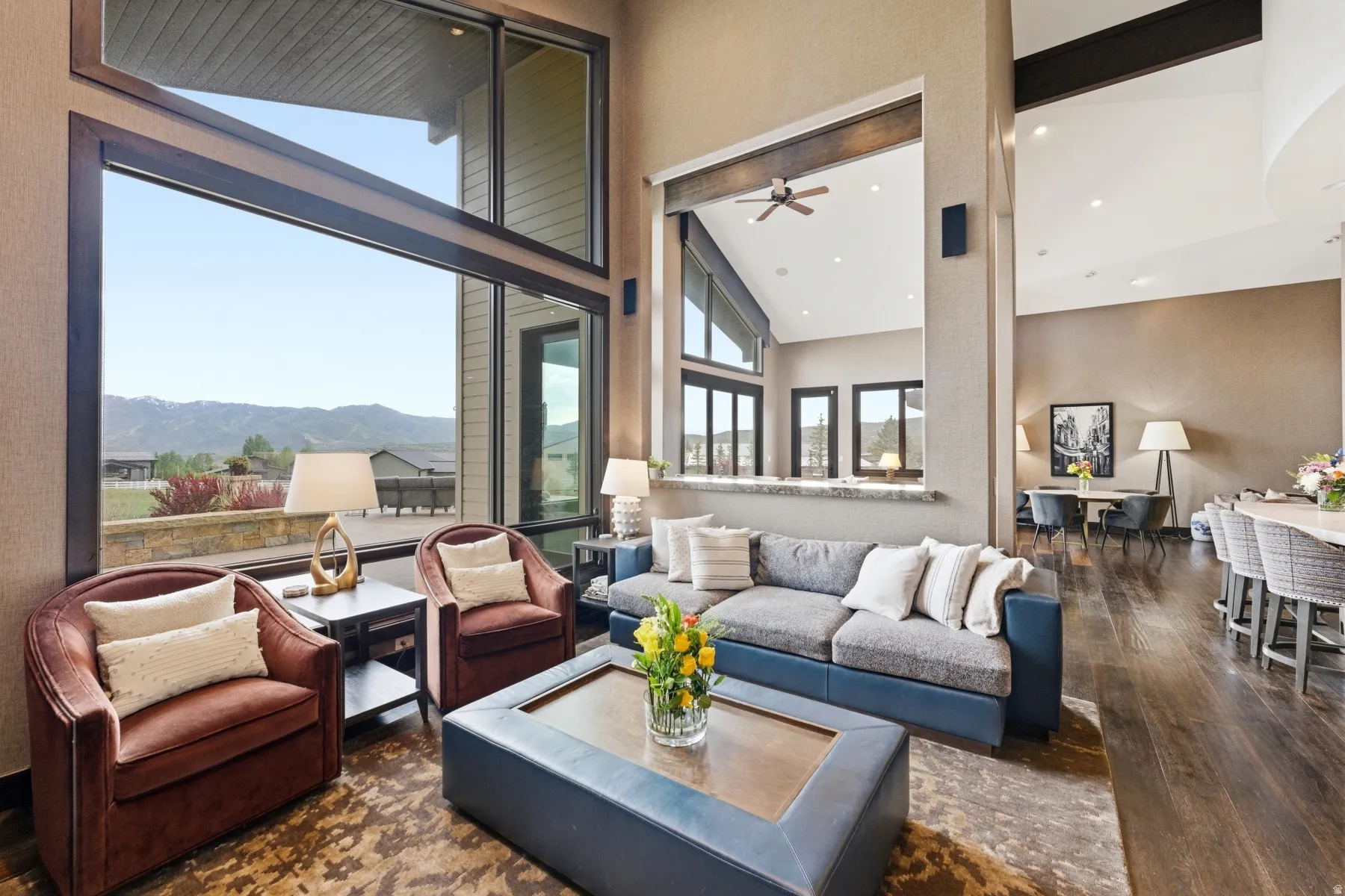 Spacious living area featuring expansive floor-to-ceiling windows, soaring vaulted ceilings, rich wood-finish flooring, and a large stone countertop bar