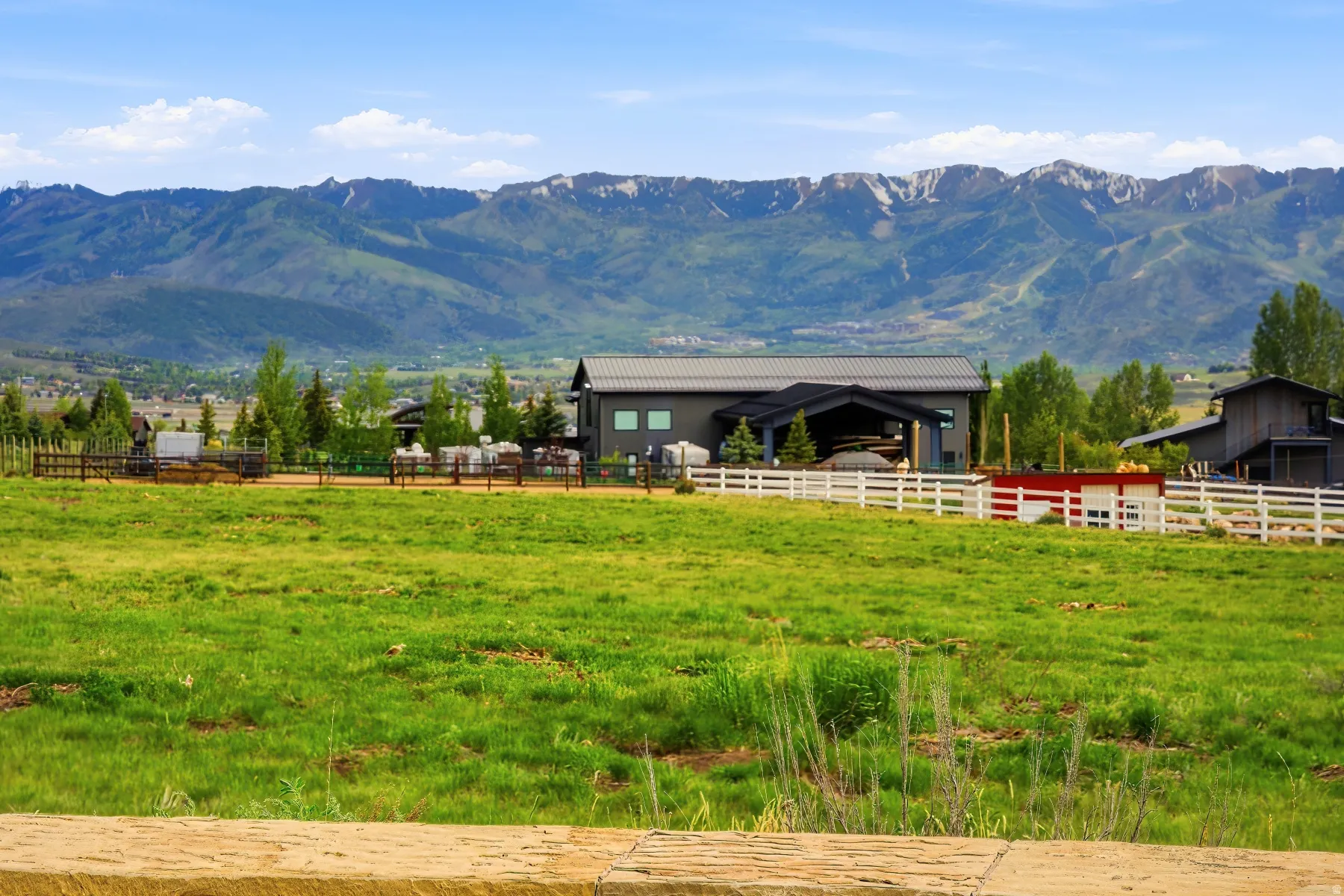 Contemporary style property featuring a large open field, a white picket fence, and a backdrop of mountainous terrain