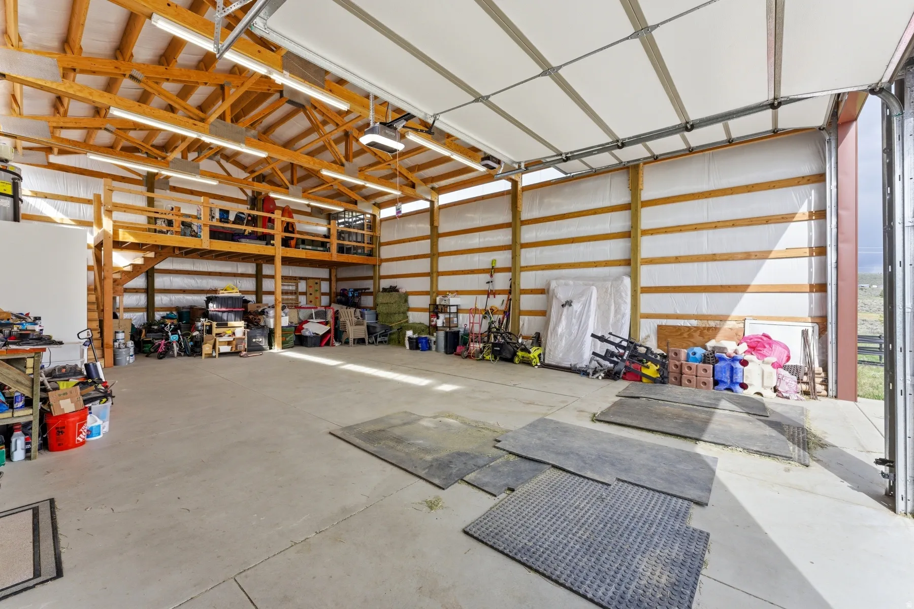 Spacious utility building featuring a concrete floor, exposed wood beam ceiling, and a large overhead door