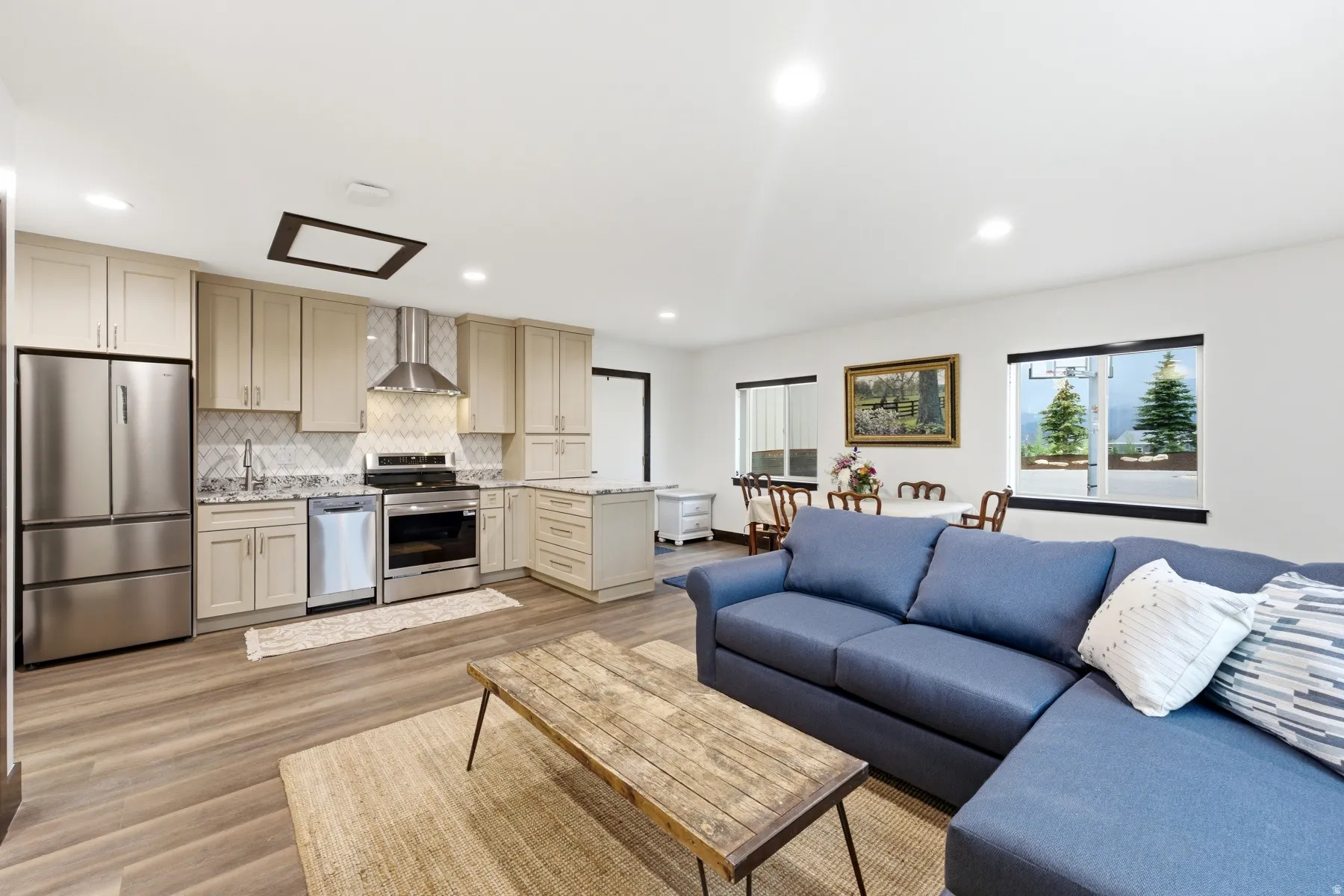Open-concept living space featuring a modern kitchen with stainless steel appliances, light-toned cabinetry, and granite countertops