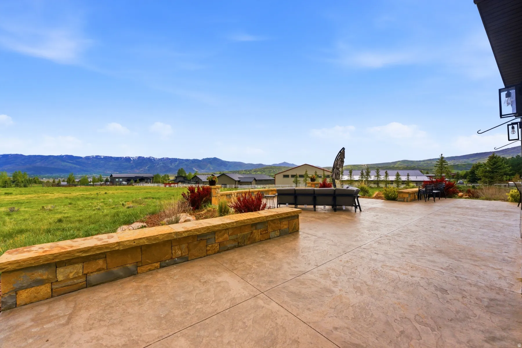 Expansive stamped concrete patio featuring a stone veneer retaining wall and landscaping with red-leafed shrubs