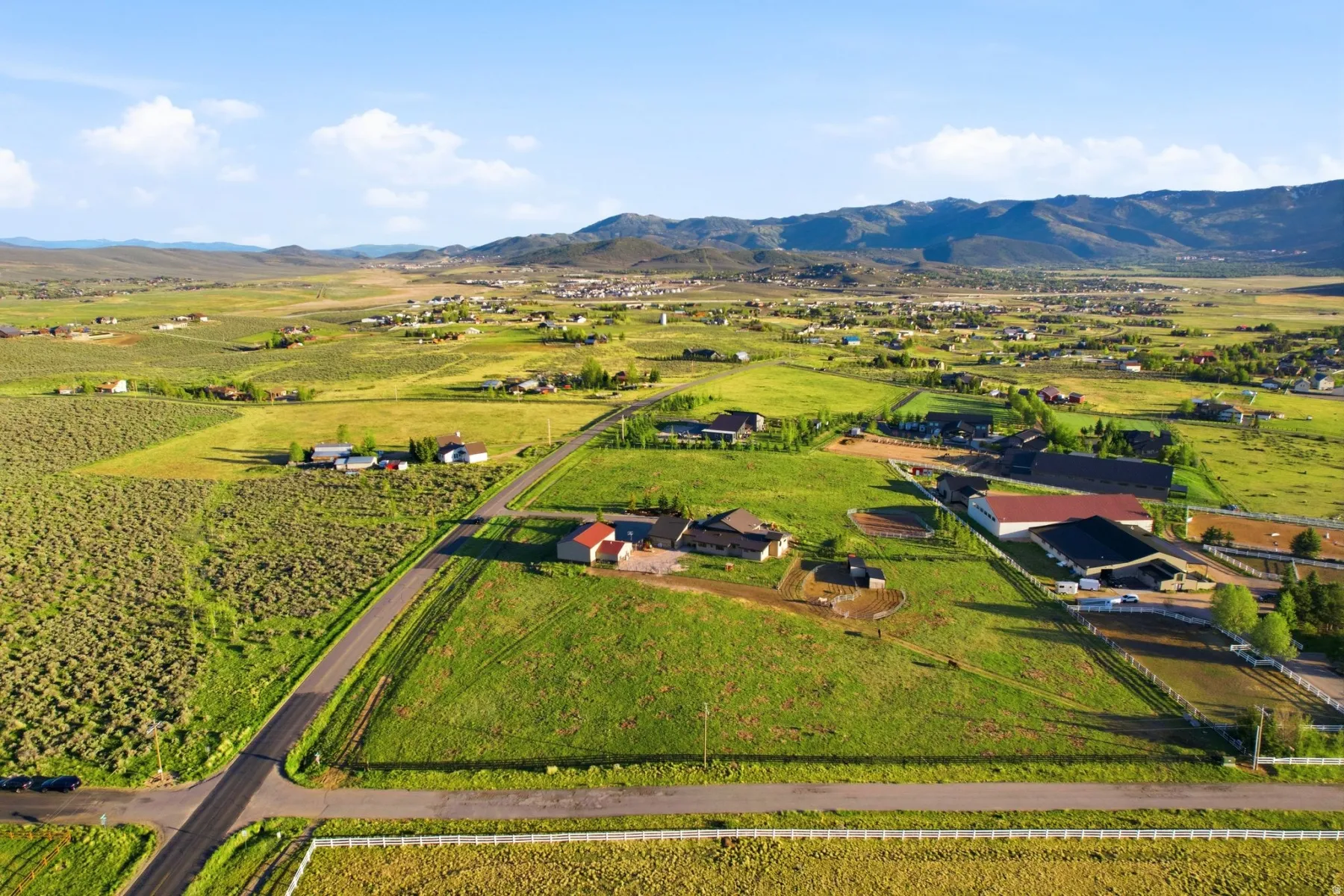 Expansive rural landscape featuring a paved road, scattered residences, agricultural fields, and distant mountains