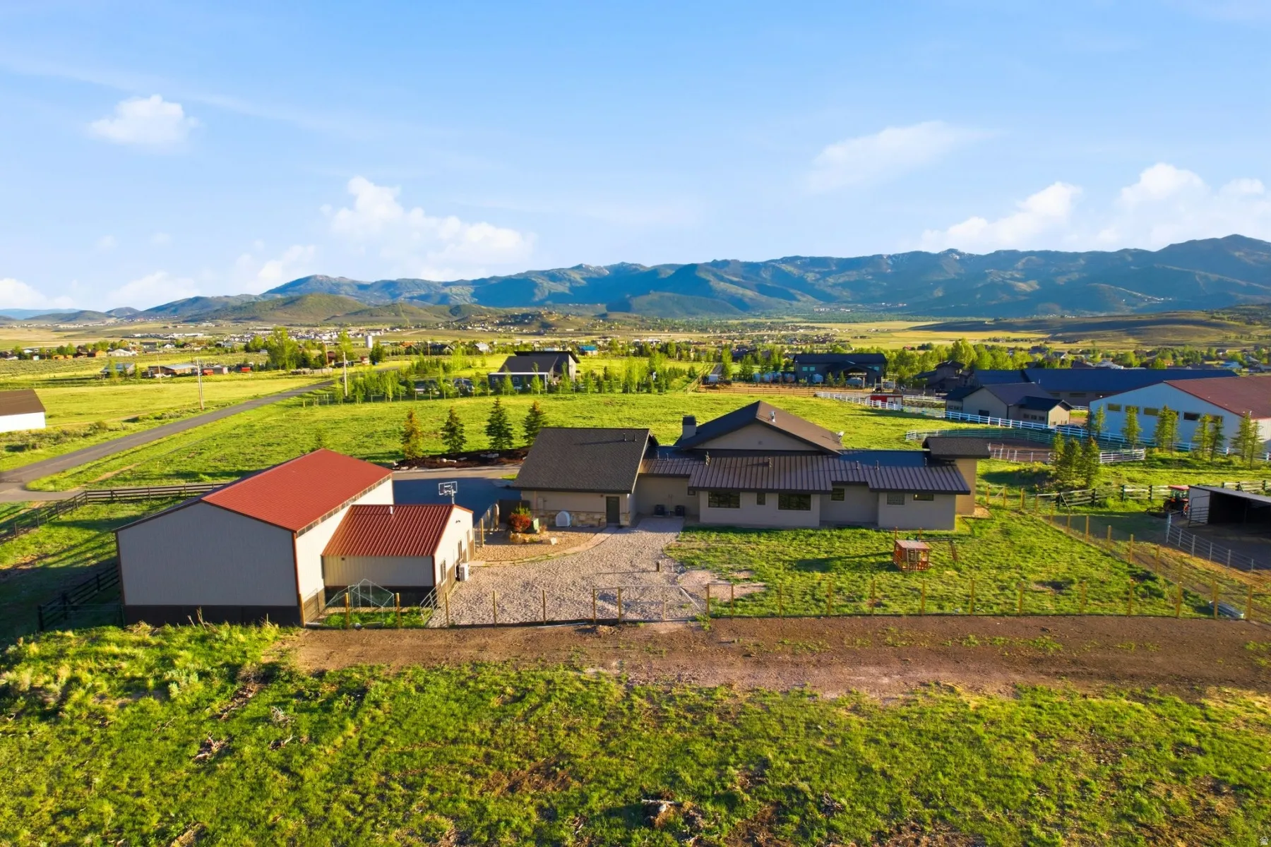 Expansive property featuring a contemporary residence, a large barn with a red roof, a separate outbuilding, and fenced pasture areas