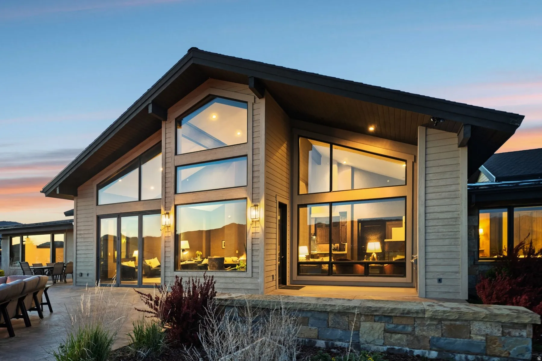 Contemporary architectural design featuring large, multi-pane windows, a stone-faced retaining wall, and an expansive concrete patio