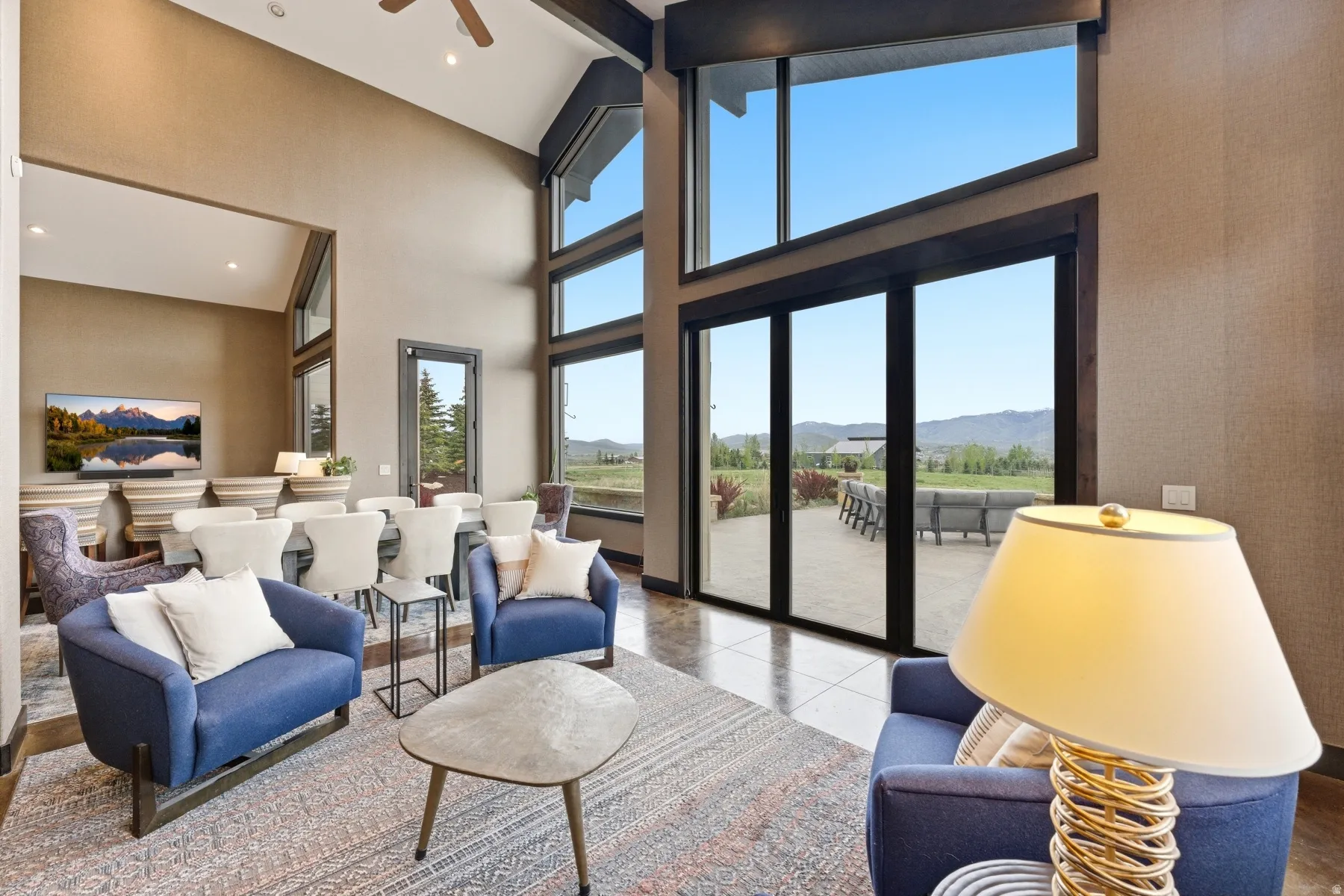 Great room featuring vaulted ceilings, exposed dark wood beams, a full wall of floor-to-ceiling glass, and large format tile flooring