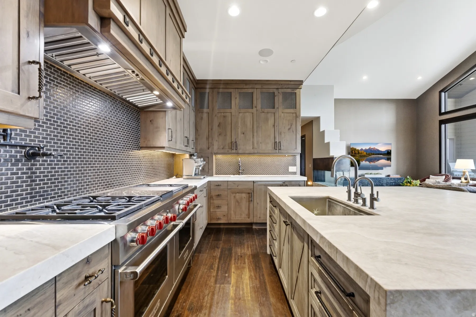 Gourmet kitchen featuring a substantial island with an undermount sink, stainless steel appliances including a range with griddle, wood-finish cabinetry, and a subway tile backsplash
