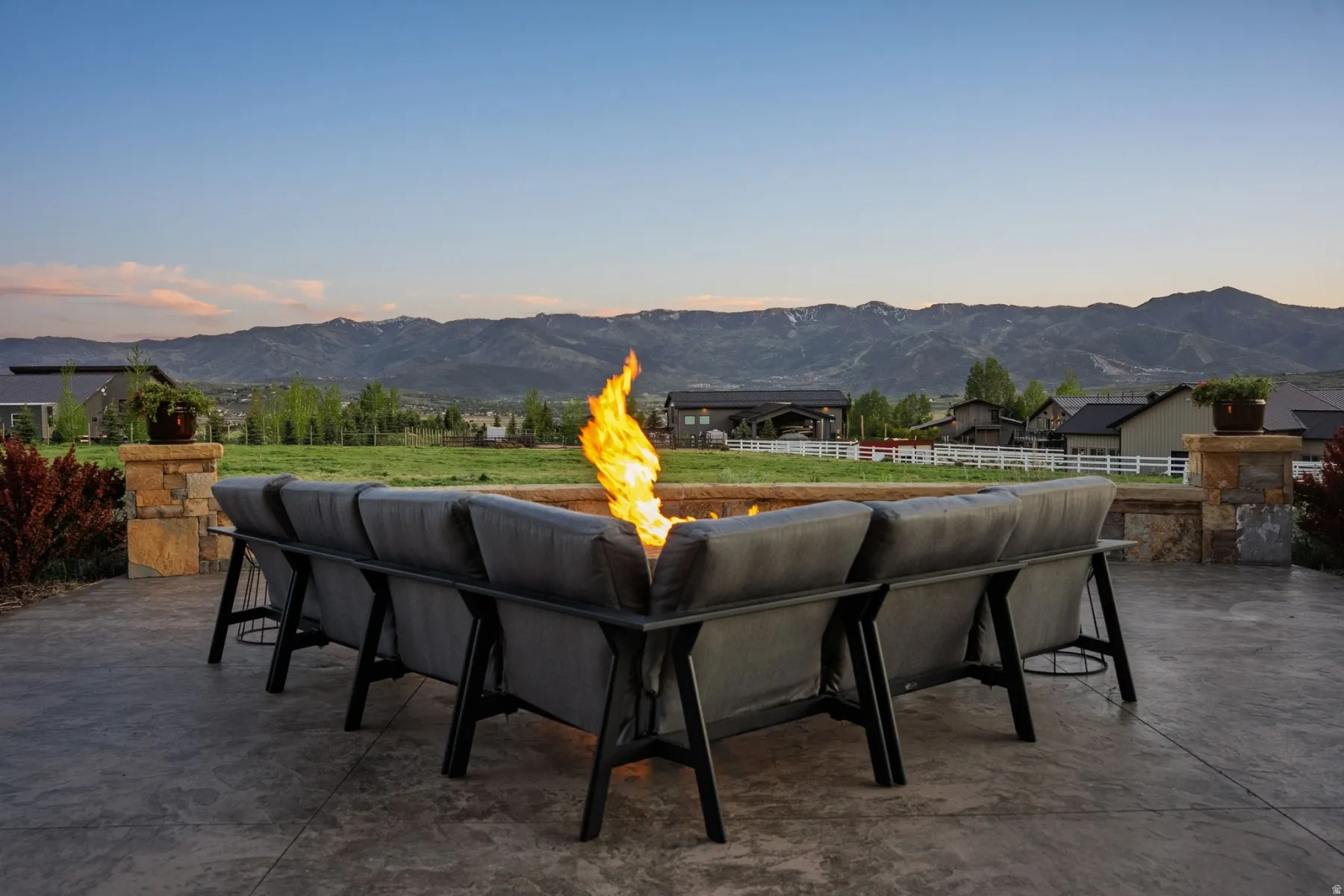 Stamped concrete patio with a built-in fire pit, stone pillar accents, and a large open field
