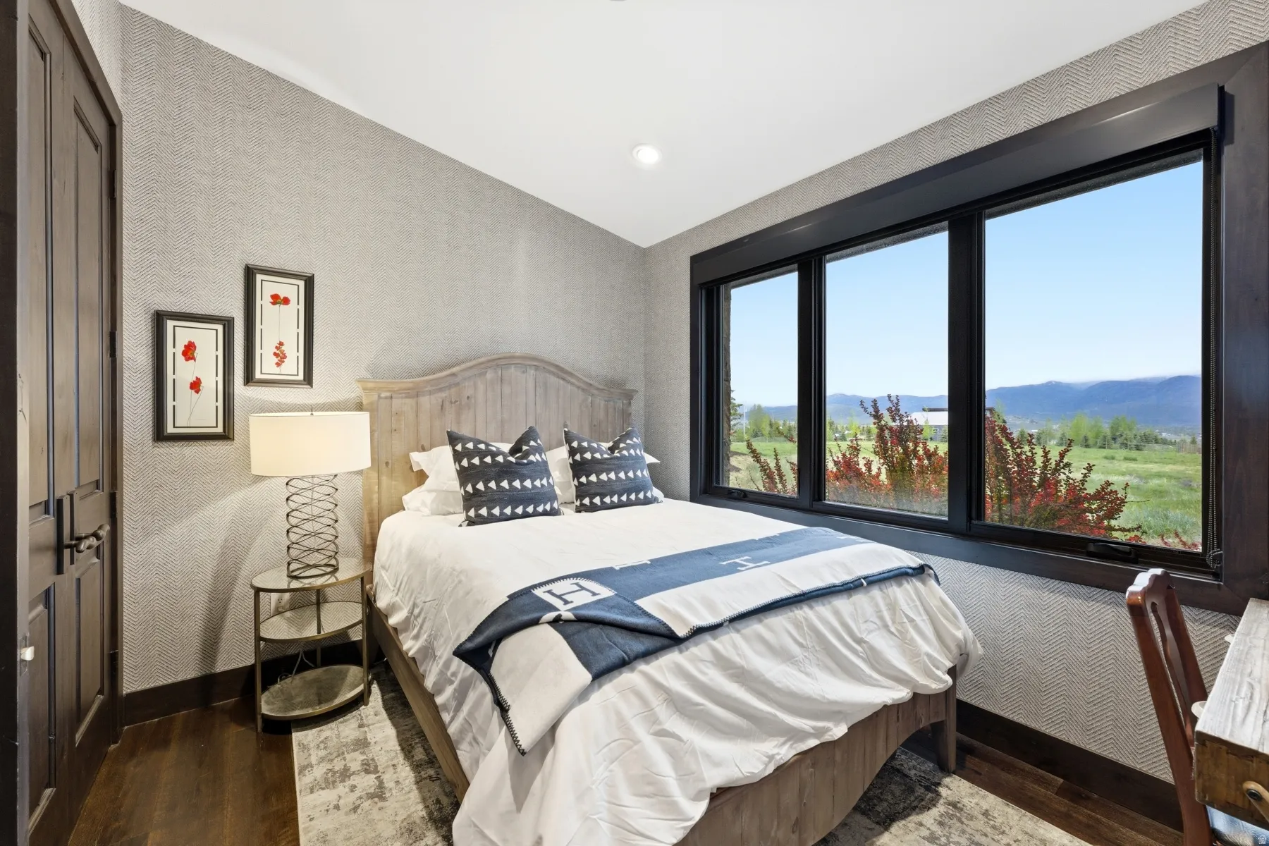 Room featuring three large windows showcasing a mountain and field landscape