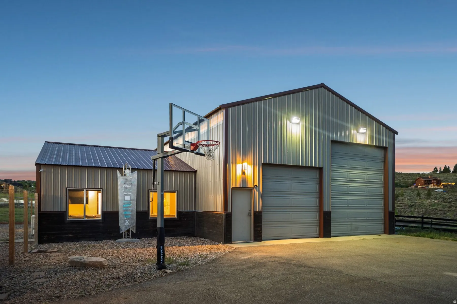 Metal-sided structure featuring two roll-up garage doors, a side entry door, and a built-in basketball hoop