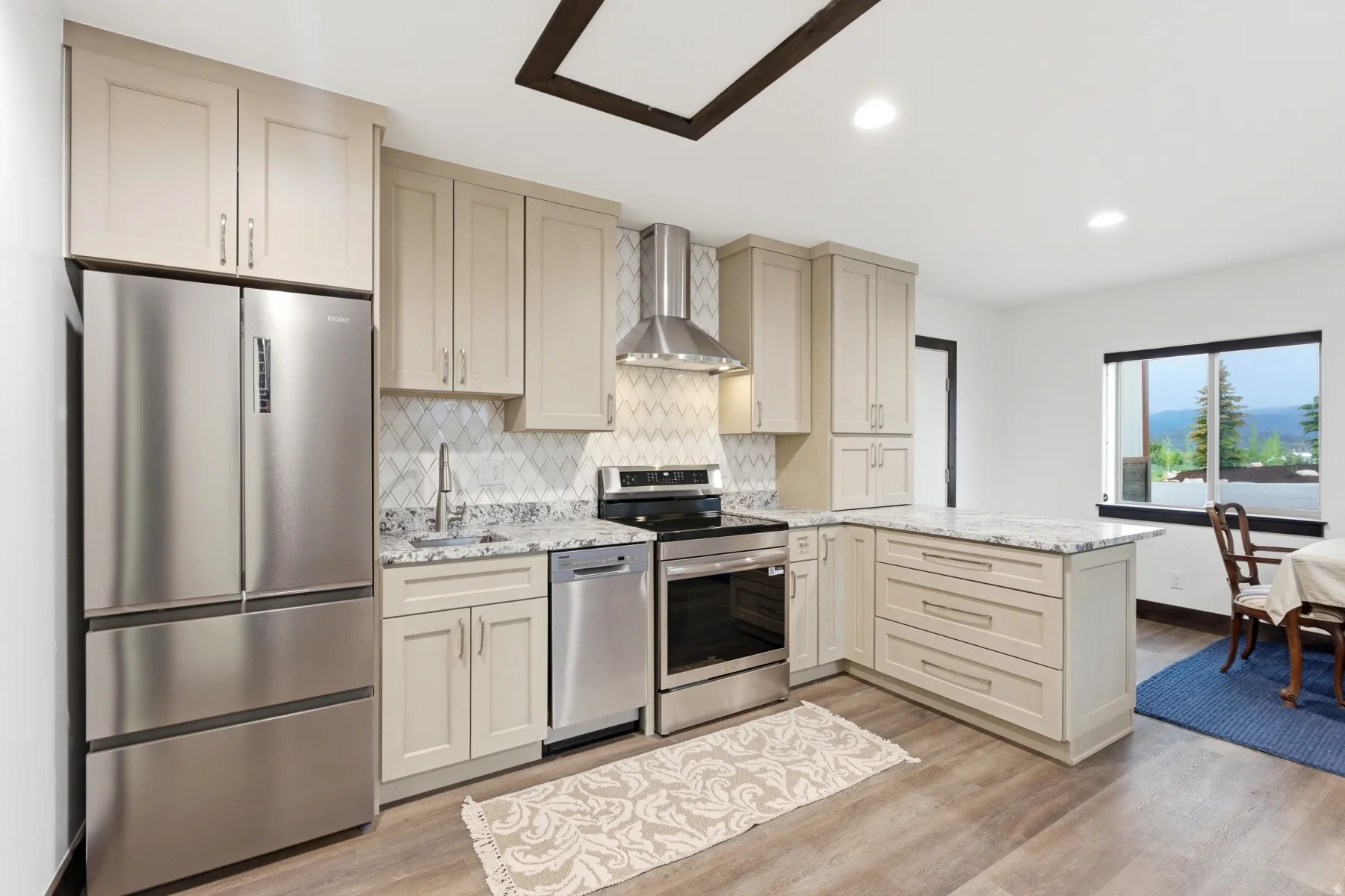 Modern kitchen featuring light-toned cabinetry, stainless steel appliances, a diamond-patterned backsplash, and a functional kitchen island