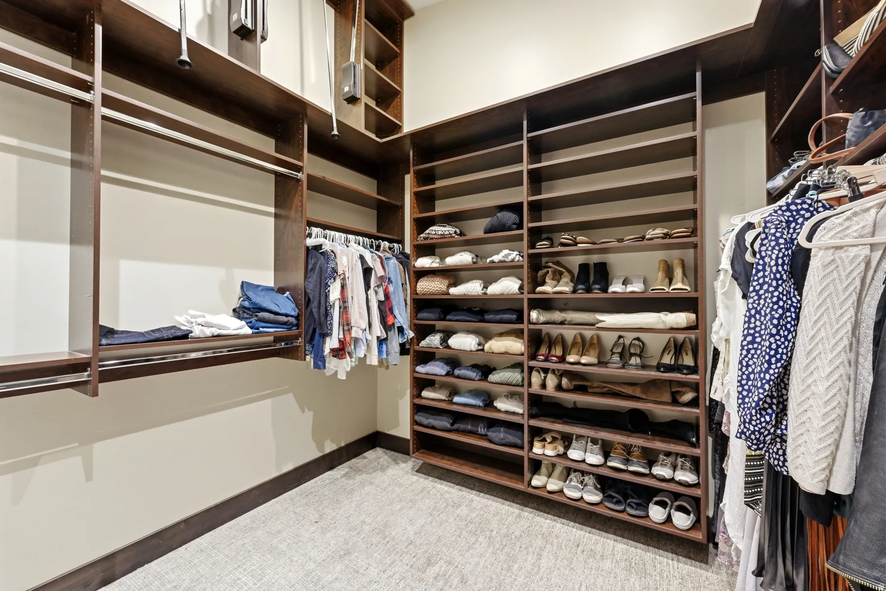 Custom closet system featuring dark wood-finish shelving, multiple hanging rods, built-in shoe racks, and light neutral-toned walls