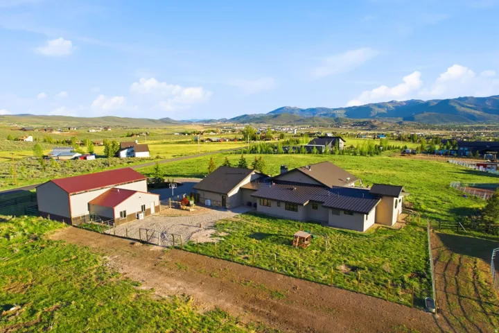 Expansive property featuring a contemporary residence with a metal roof, a large outbuilding with a red metal roof, and a separate structure with a matching red metal roof