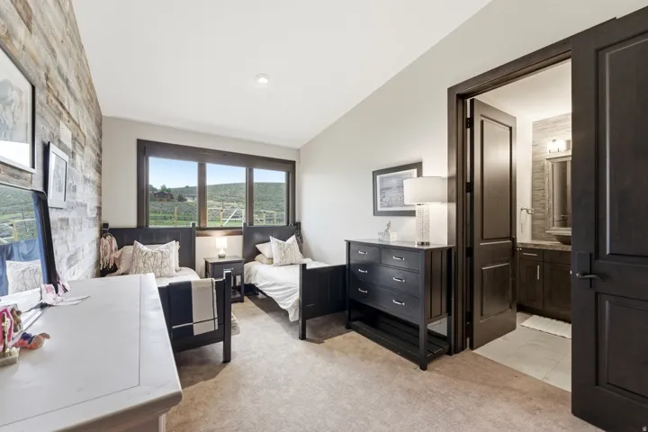 Bedroom featuring a reclaimed wood accent wall, broad windows framing a rural landscape, and plush carpet flooring