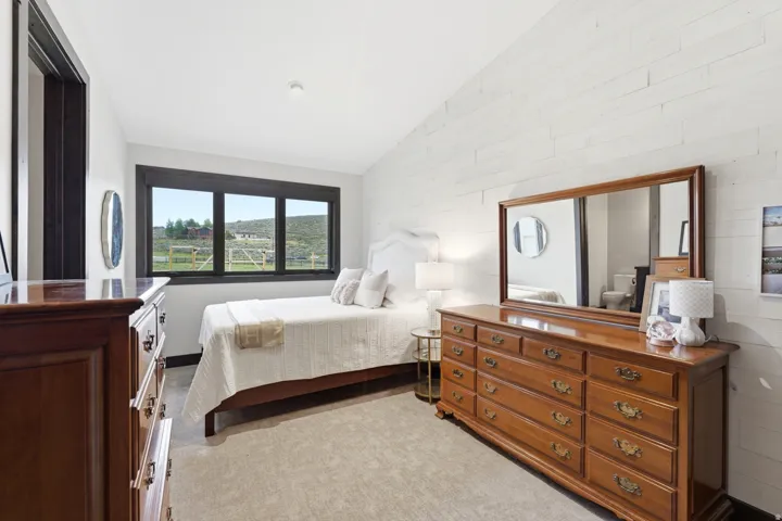 Bedroom with a large black-framed window, light-colored plank wall accent, dark wood-finish door casing, and neutral-toned carpeting