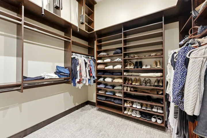 Custom closet system featuring dark wood-finish shelving, multiple hanging rods, built-in shoe racks, and light neutral-toned walls