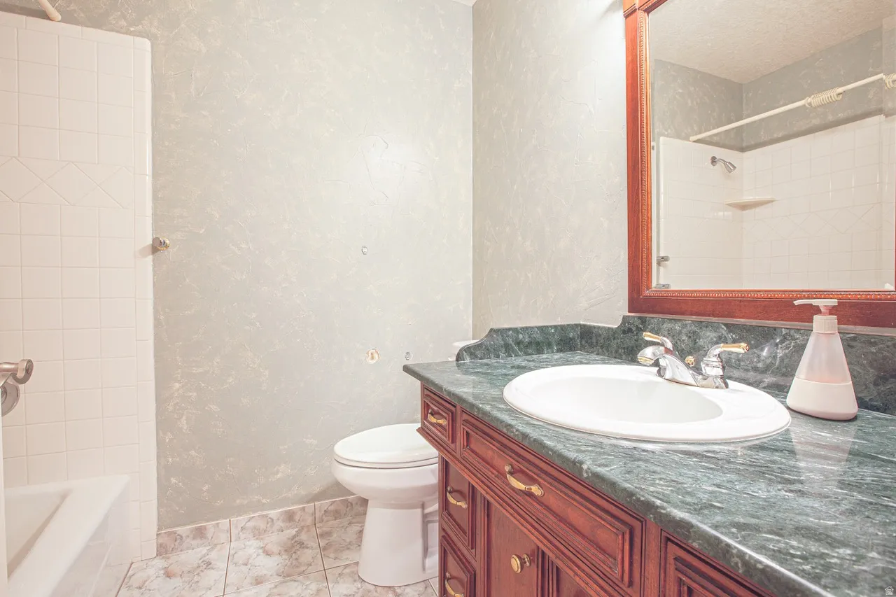 Bathroom featuring a vanity with a green countertop, an undermount sink, and a wood-finish cabinet with brass-tone hardware