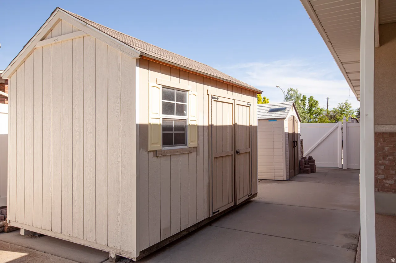 Two outdoor storage sheds on a concrete pad, featuring a paneled exterior, gable roofs, and a window with shutters on the foreground shed