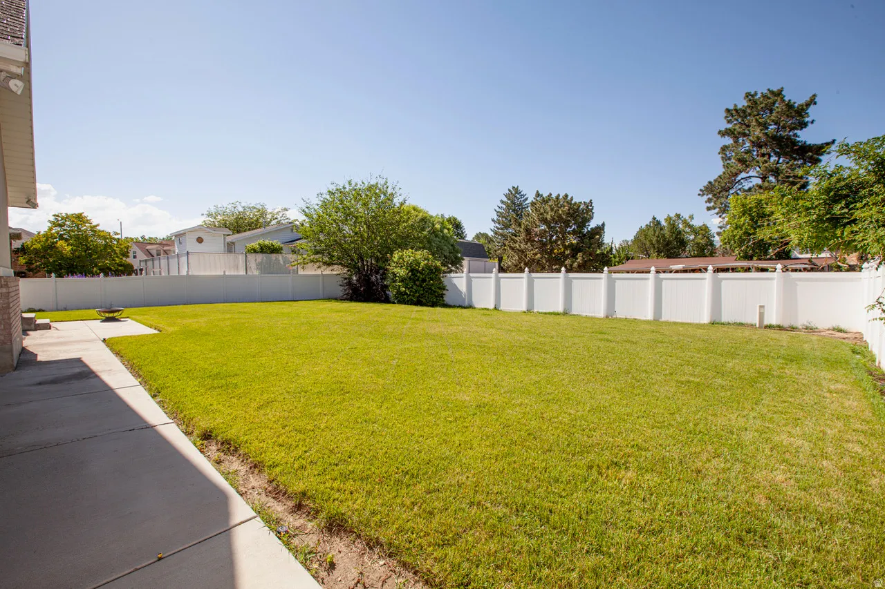 Expansive backyard featuring a lush lawn, concrete patio, and mature trees