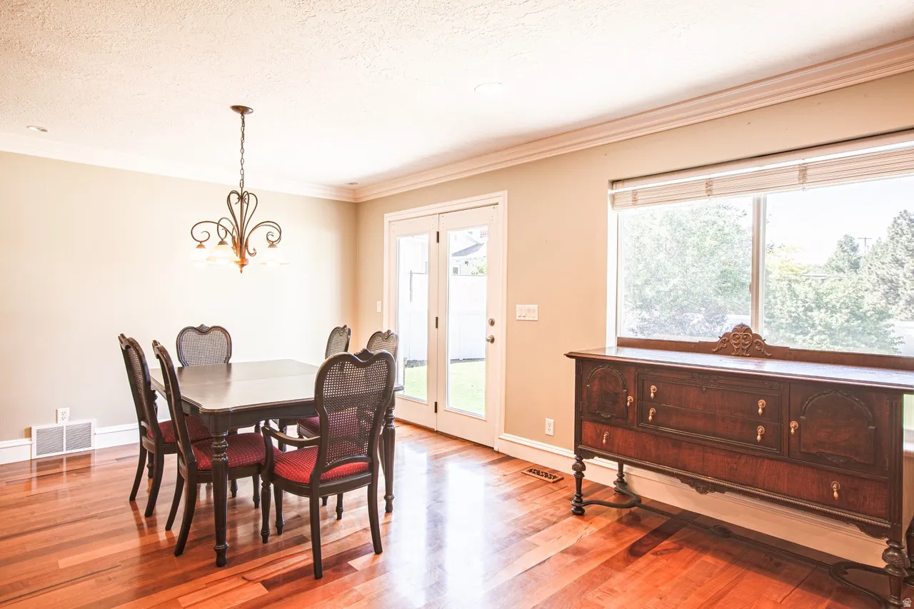 Dining area featuring wood-finish flooring, crown molding, a decorative chandelier, and French doors opening to an exterior space