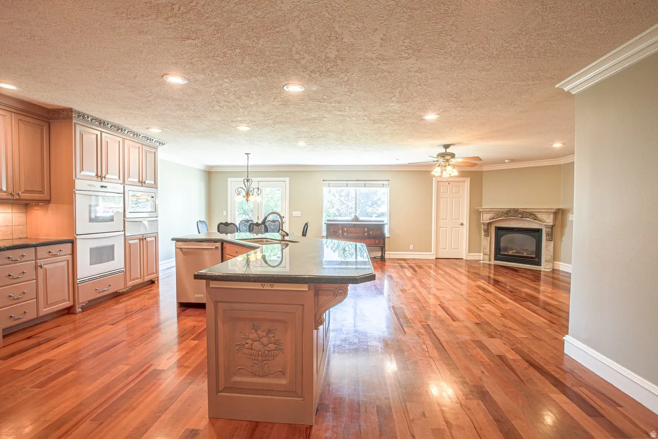 Spacious interior featuring wood-finish flooring, a kitchen island with seating, integrated double ovens, a decorative fireplace with a stone mantel, and recessed lighting