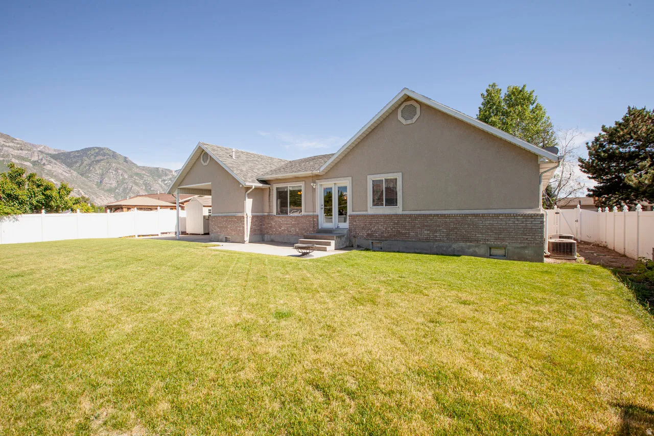 Expansive backyard featuring a large green lawn, concrete patio, and white vinyl perimeter fencing