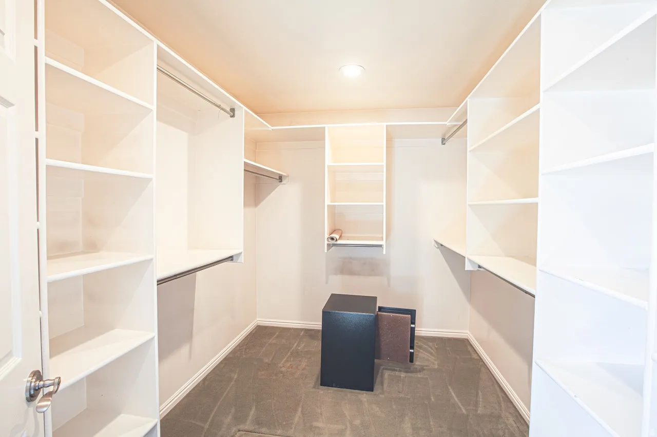 Spacious walk-in closet featuring extensive built-in shelving, multiple hanging rods, recessed lighting, and a neutral wall color