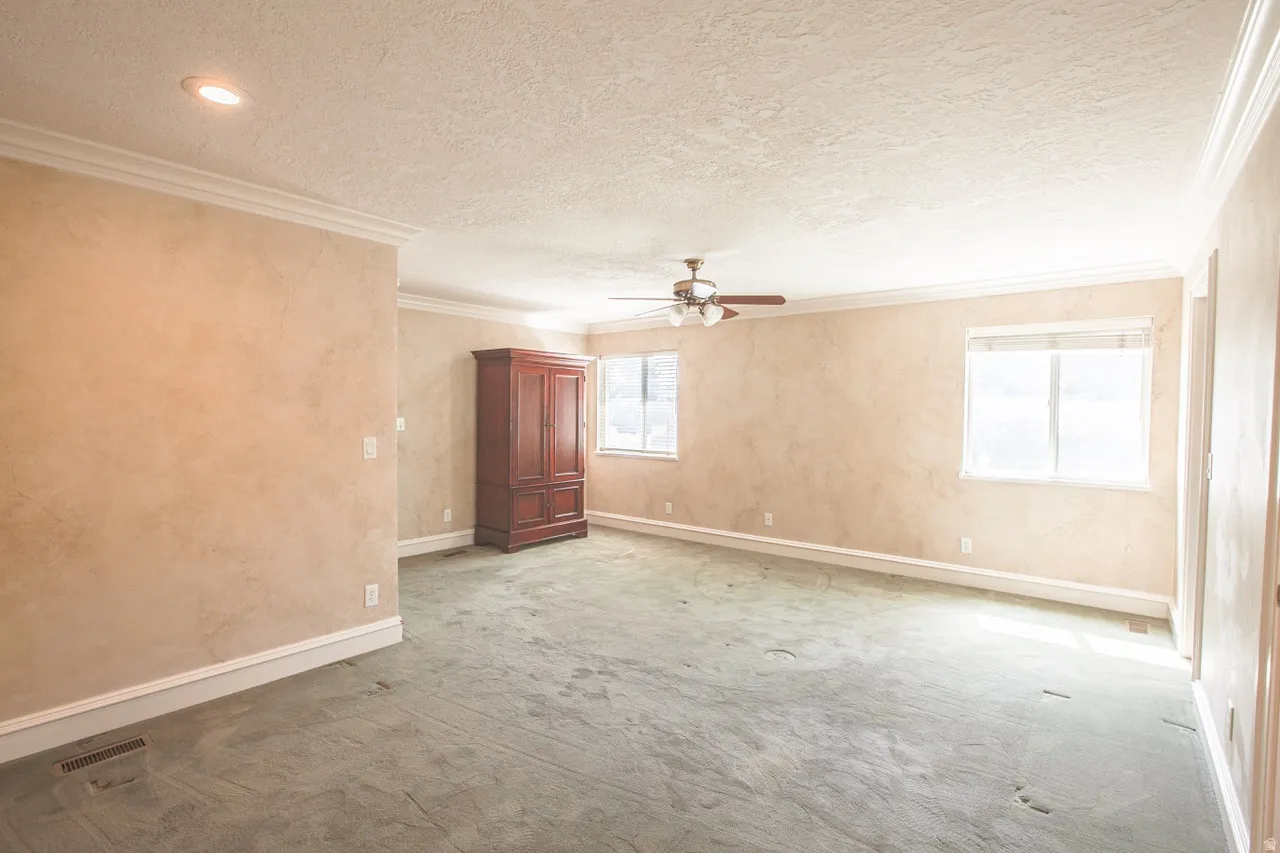 Spacious room featuring multiple windows, a ceiling fan with integrated lighting, recessed lighting, and crown molding