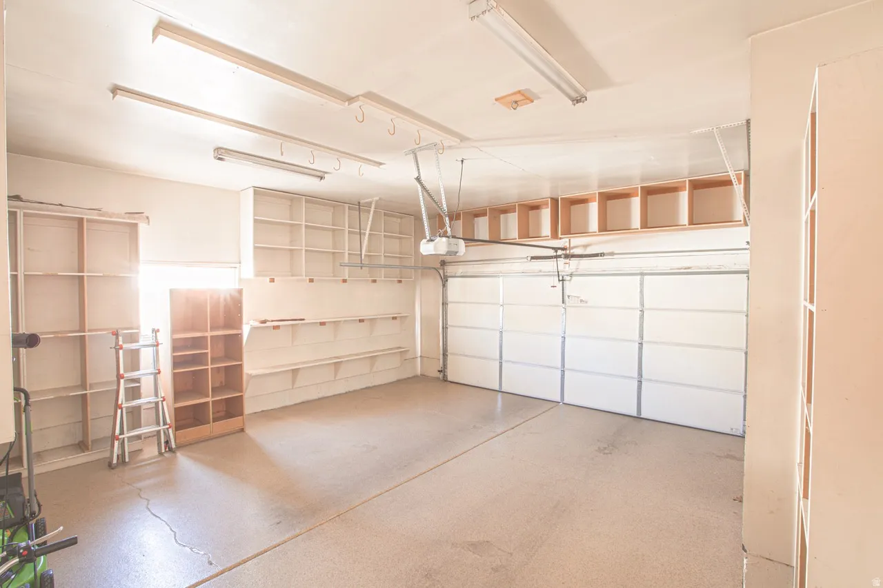 Spacious garage featuring a paneled garage door, fluorescent overhead lighting, extensive built-in shelving, and an automatic garage door opener