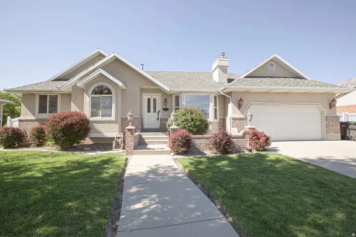 Traditional ranch-style residence featuring a stucco exterior with brick accents, an attached two-car garage, mature landscaping, a concrete walkway, and a covered entryway