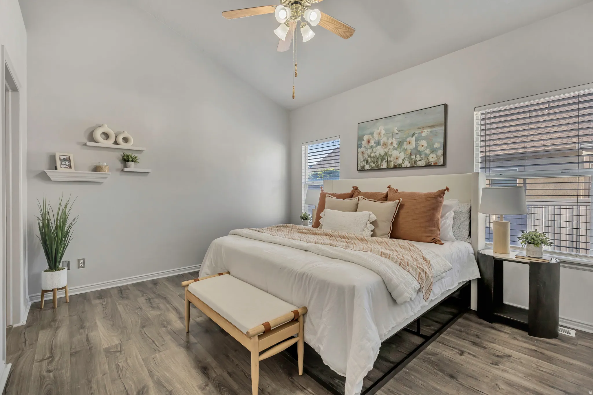 Vaulted ceiling room featuring wood-finish flooring, a ceiling fan with integrated lighting, multiple windows with blinds, and white wall shelving