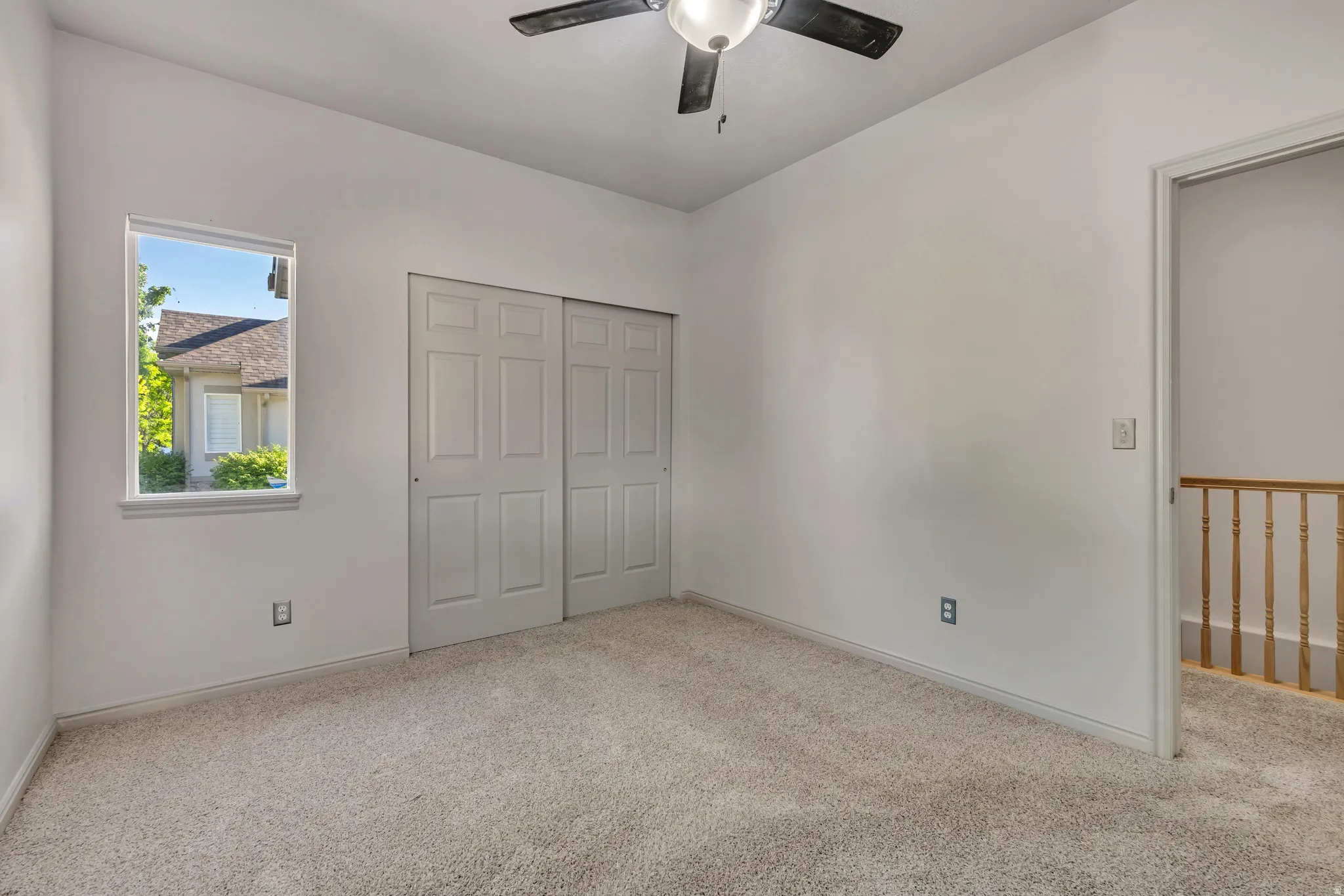 Carpeted room featuring a ceiling fan with integrated lighting, a double-panel closet with sliding doors, and a window providing natural light