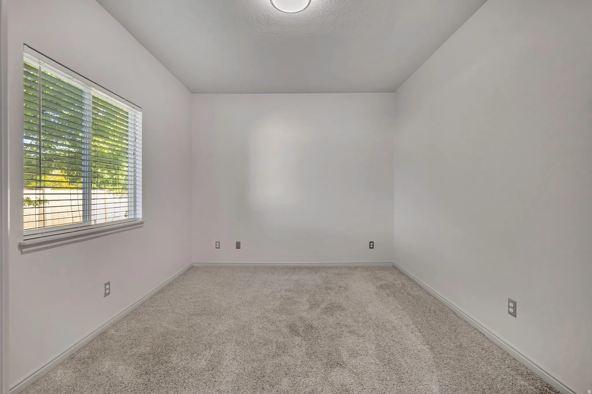 Neutral-toned wall-to-wall carpeting complements a window fitted with horizontal blinds