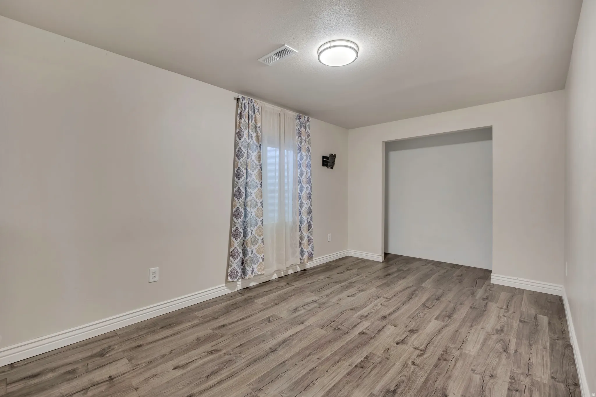 Spacious room featuring wood-finish flooring, white baseboards, and neutral wall tones