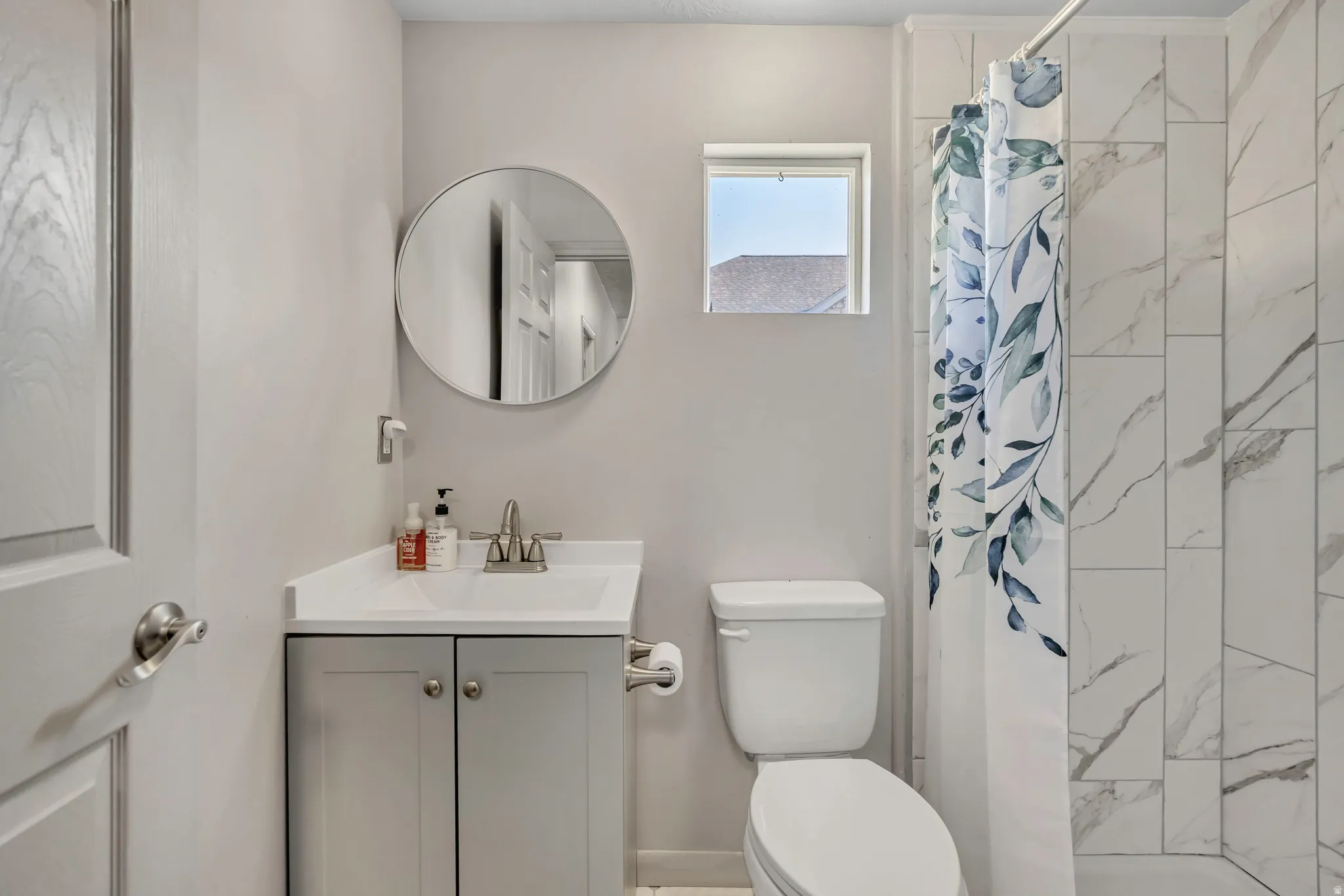 Bathroom featuring a vanity with a white countertop, a circular wall mirror, and a toilet