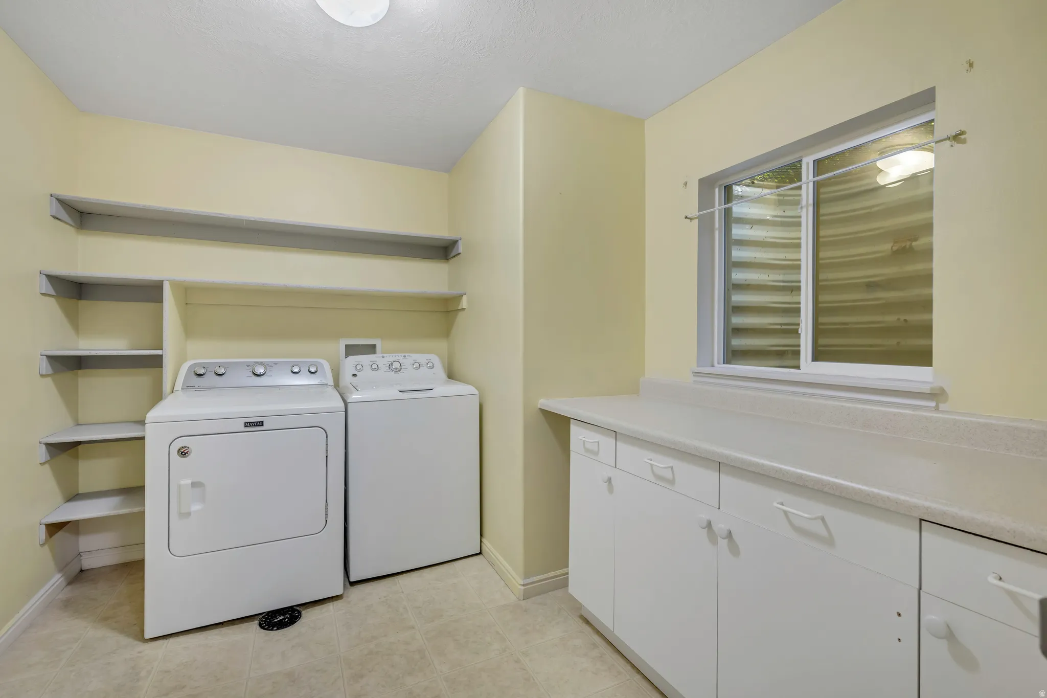 Laundry room featuring a sliding window, built-in shelving, and extensive cabinetry with countertop space