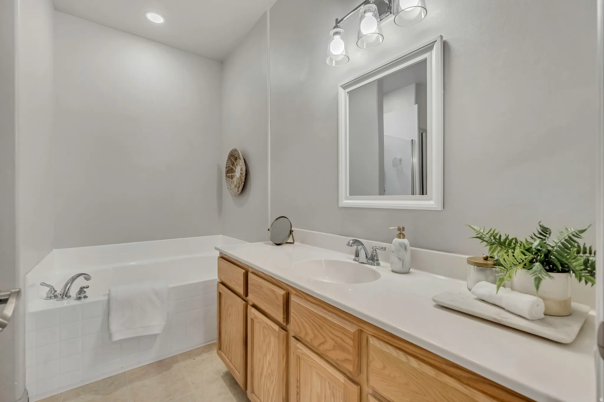 Bathroom featuring a built-in tub, a single vanity with a white countertop, wood-finish cabinetry, an undermount sink, and a framed mirror with overhead lighting