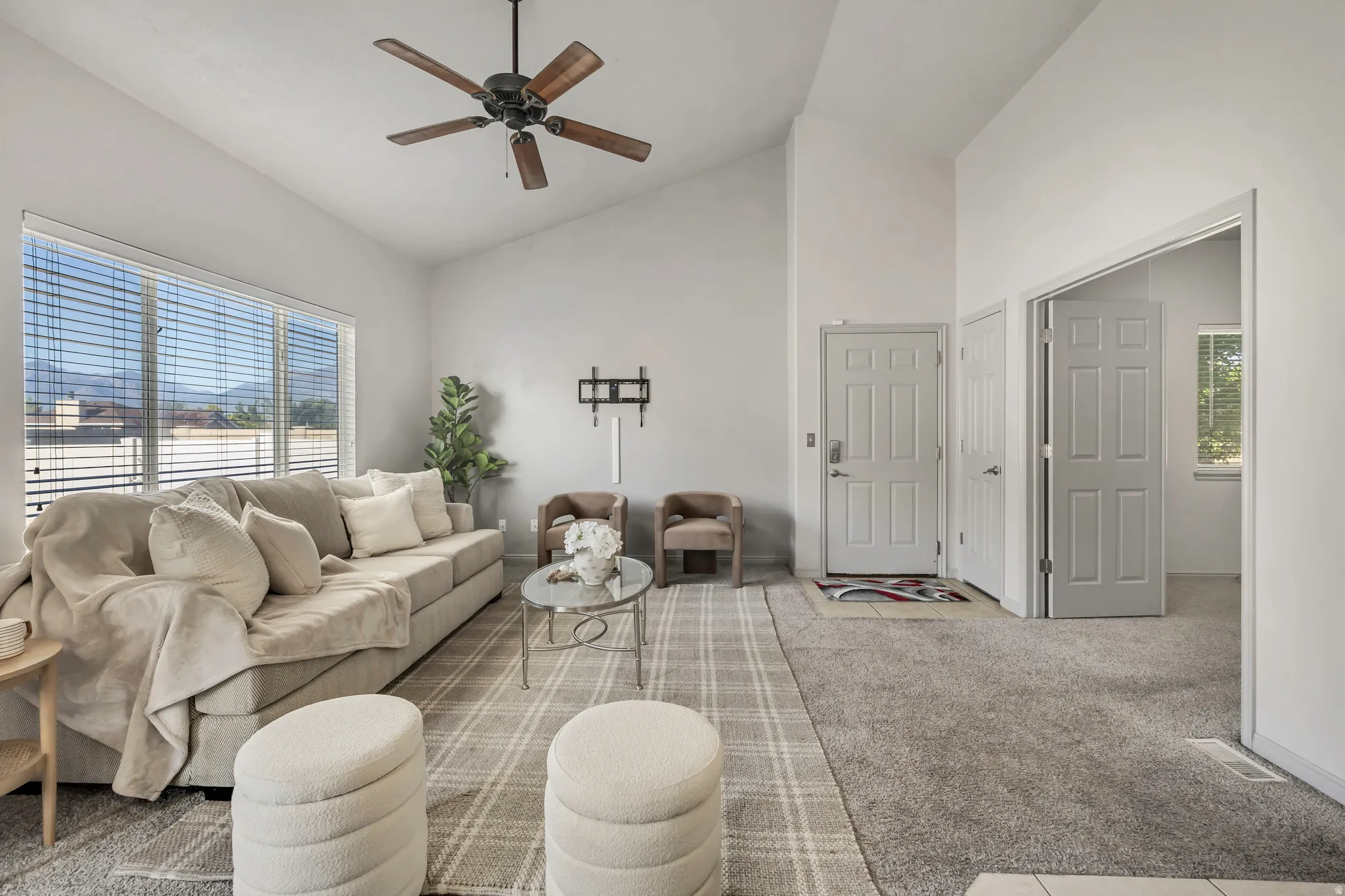 Spacious living area featuring vaulted ceilings, a ceiling fan, and large windows with horizontal blinds