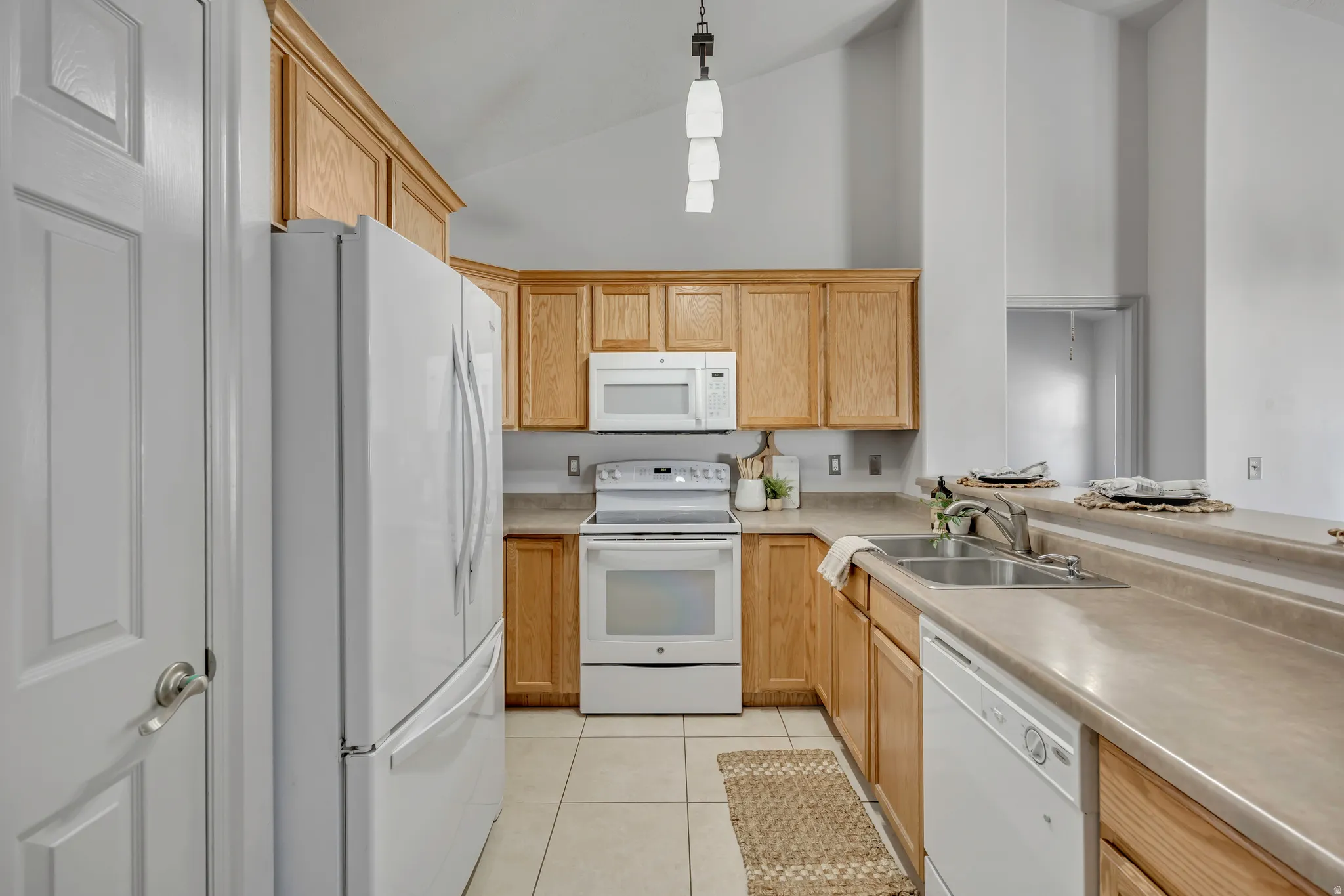Kitchen featuring wood cabinetry, white appliances, a double basin stainless steel sink, and light-toned countertops