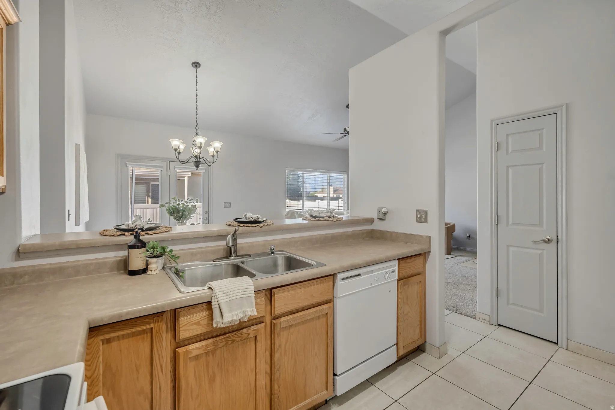 Kitchen featuring a double stainless steel sink, wood-finish cabinetry, and a white dishwasher