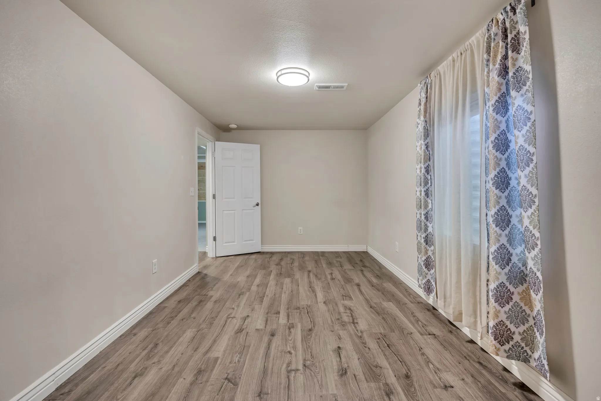 Spacious room featuring wood-finish flooring, white baseboards, and neutral wall tones