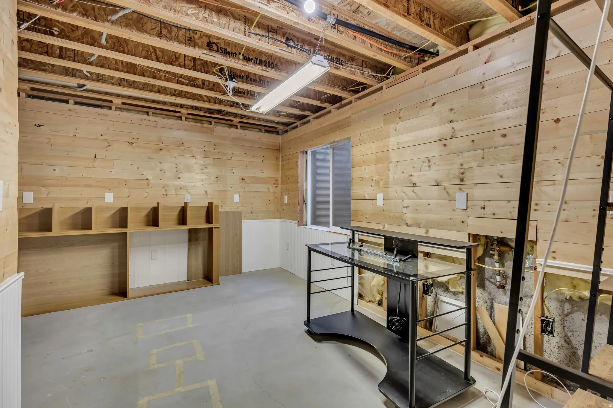 Unfinished basement space featuring exposed ceiling joists, wood plank wall paneling, and a concrete floor