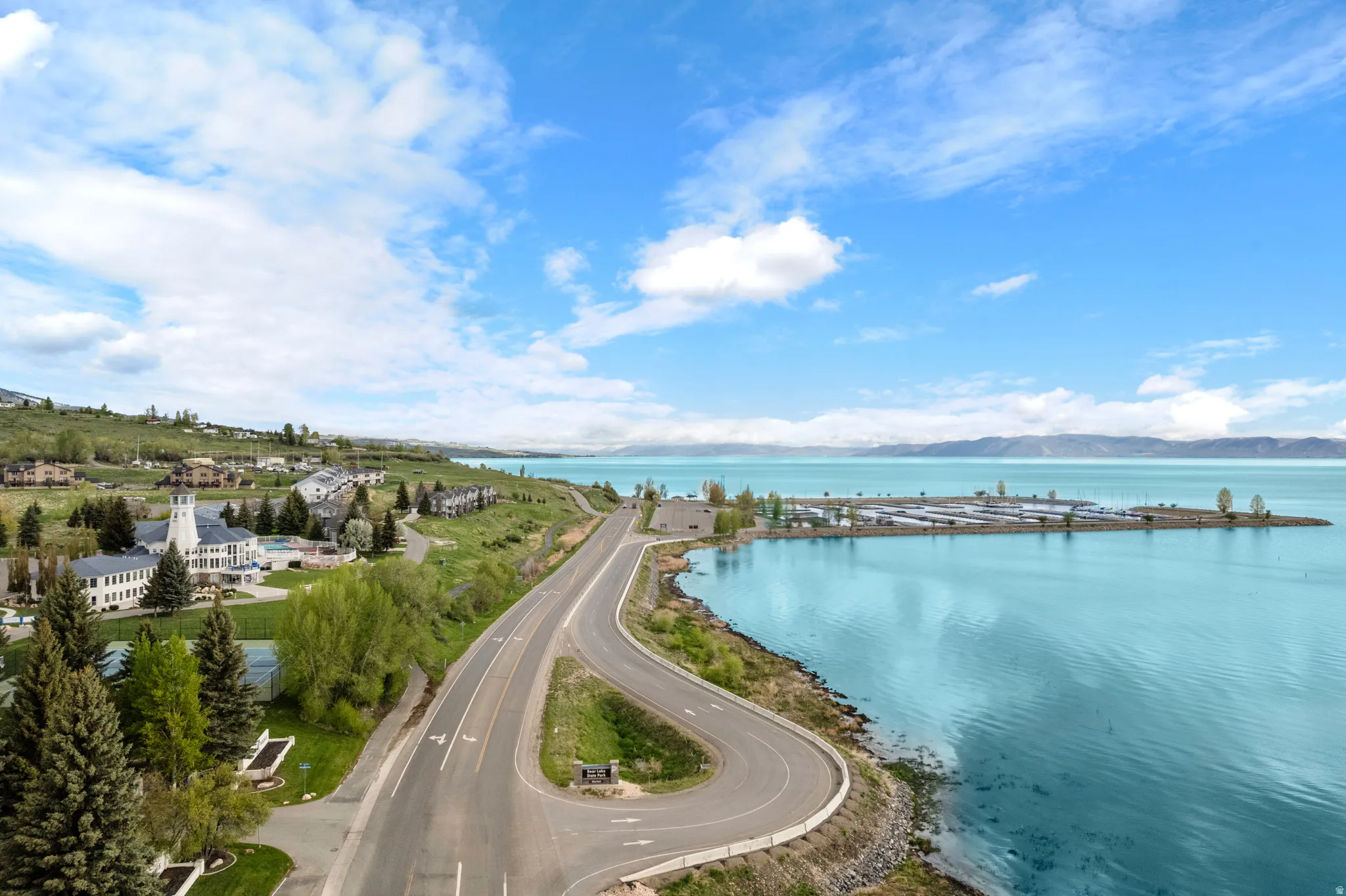 Expansive waterfront setting featuring a marina, a winding roadway, and a distant mountain range