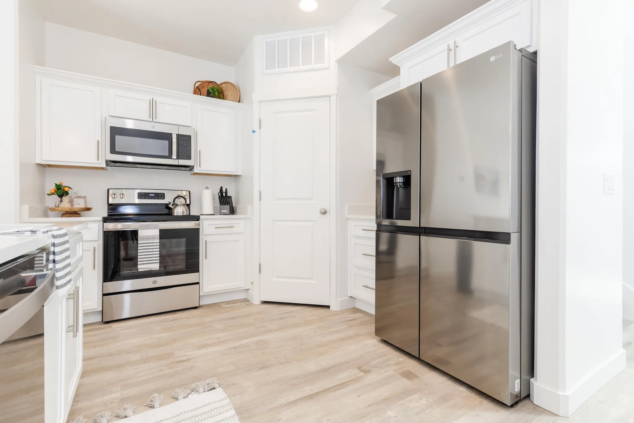 Modern kitchen featuring white shaker cabinetry with brushed nickel hardware, stainless steel appliances, light-toned wood-finish flooring, and white countertops