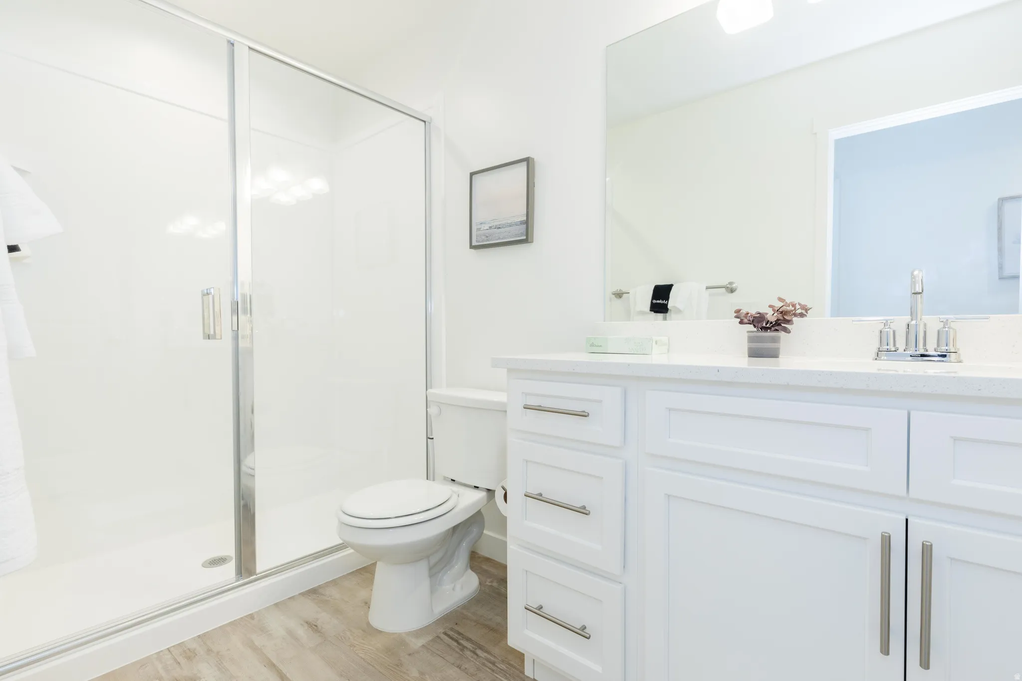 Bathroom featuring a glass-enclosed shower, white vanity with shaker-style cabinetry, quartz countertop, and wood-finish flooring