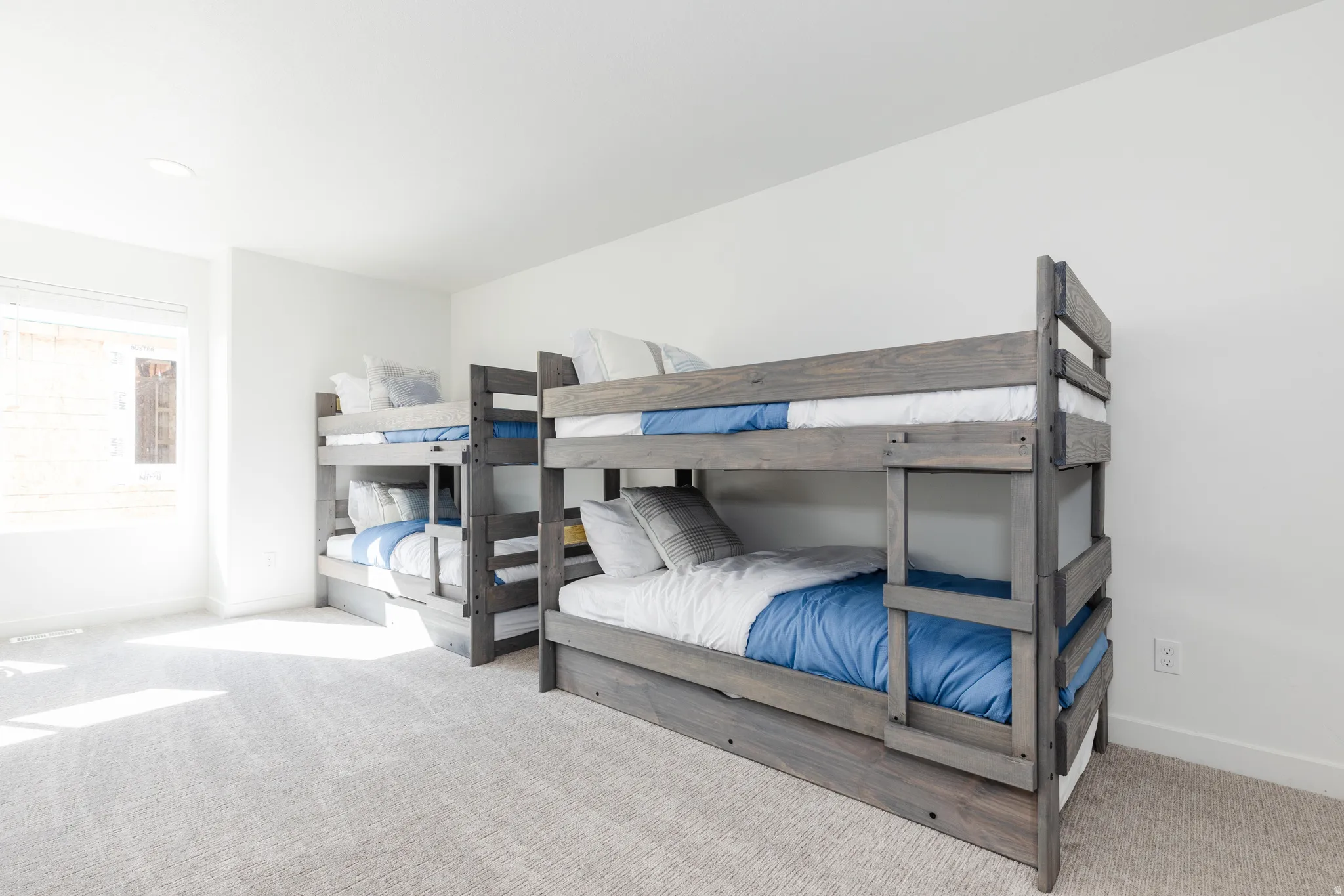 Spacious room featuring two bunk beds with a weathered wood finish, light-colored carpeting, a large window, and recessed lighting