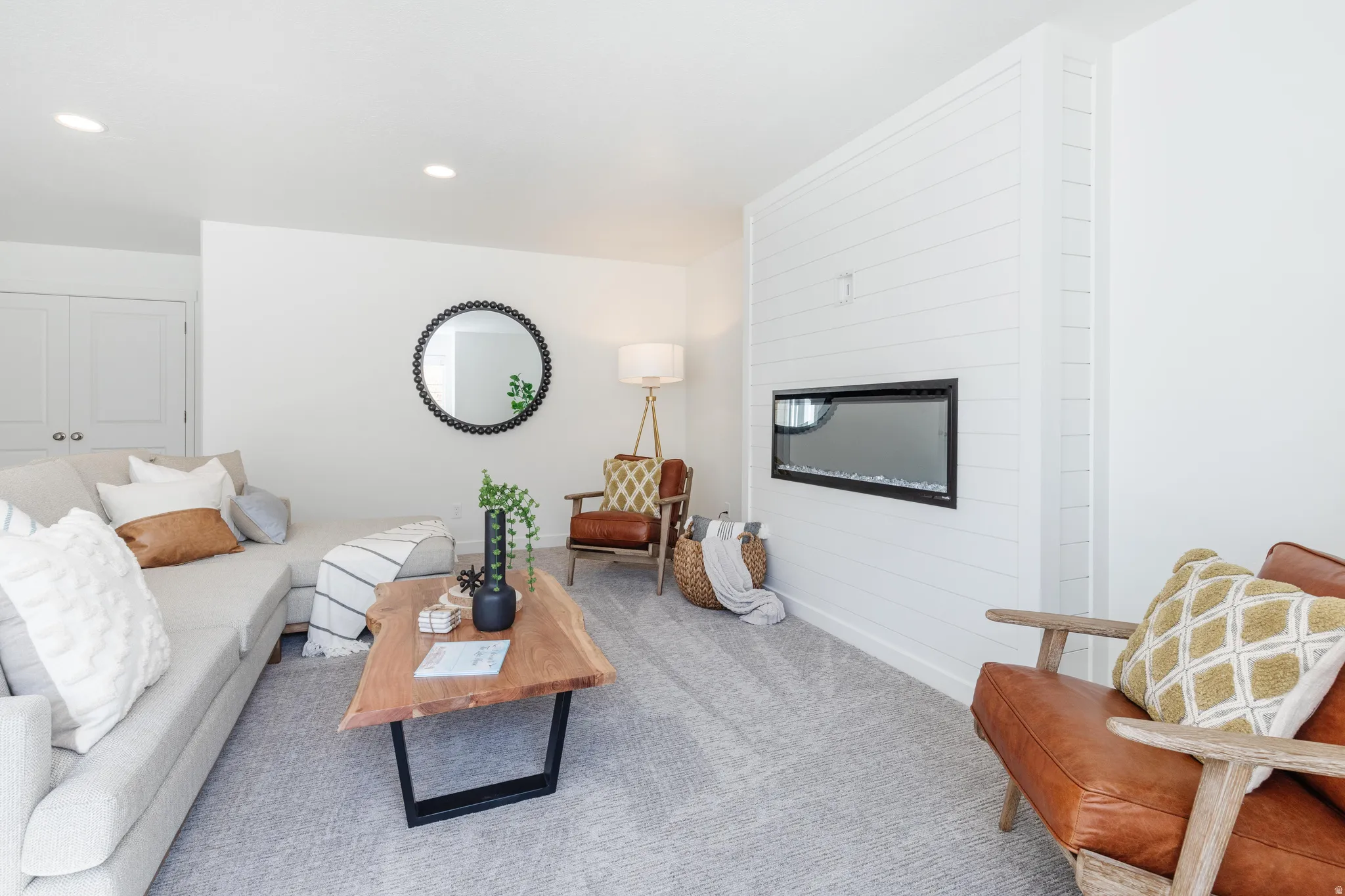 Living area featuring a shiplap accent wall with a built-in linear electric fireplace, soft gray carpeting, recessed ceiling lighting, and crisp white walls