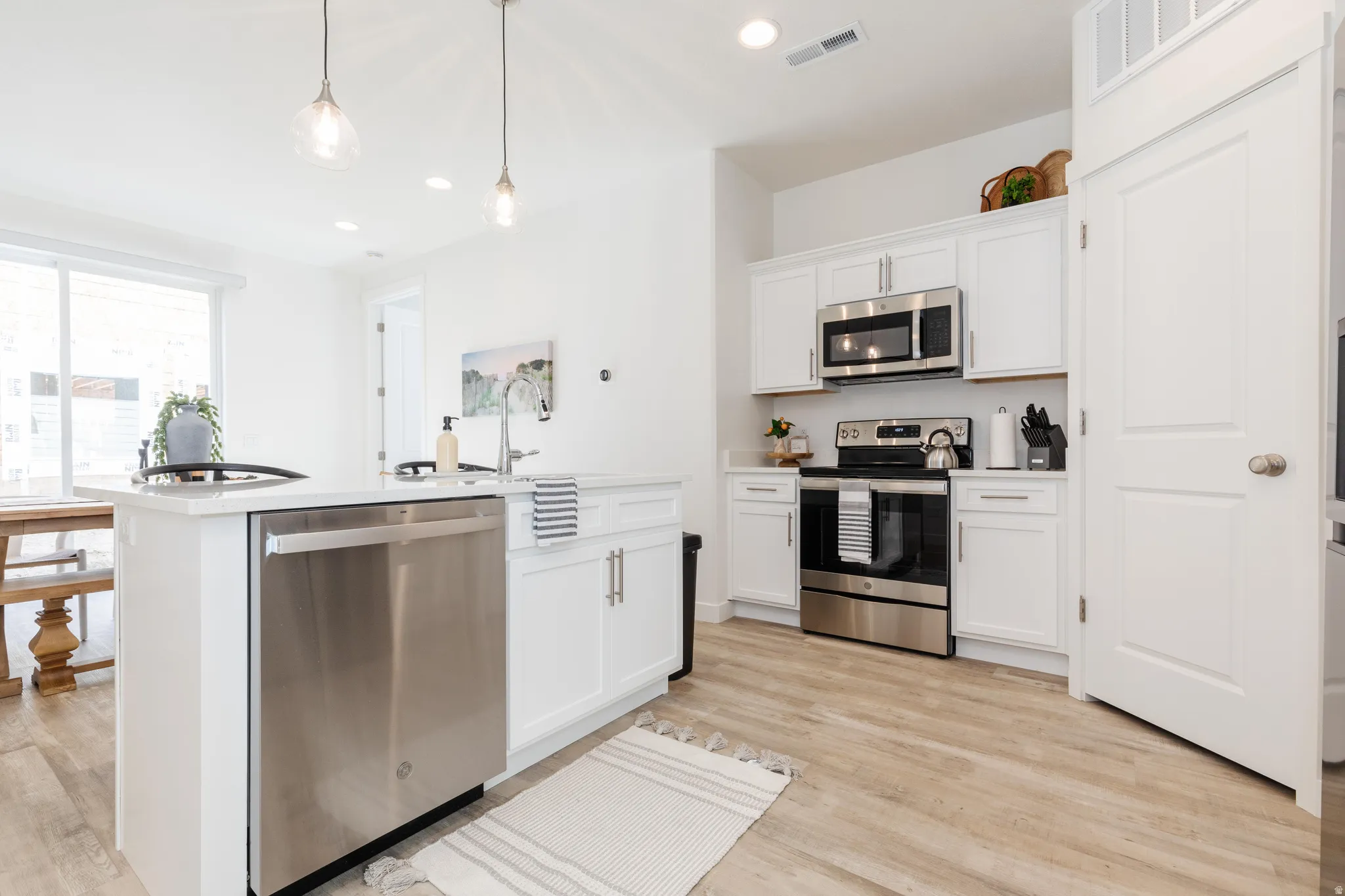 Contemporary kitchen featuring white cabinetry, stainless steel appliances, and wood-finish flooring