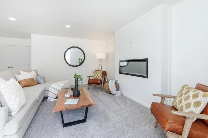Living area featuring a shiplap accent wall with a built-in linear electric fireplace, soft gray carpeting, recessed ceiling lighting, and crisp white walls