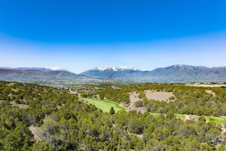 Expansive golf course property featuring a lush green fairway, natural landscape with numerous trees, and distant snow-capped mountains