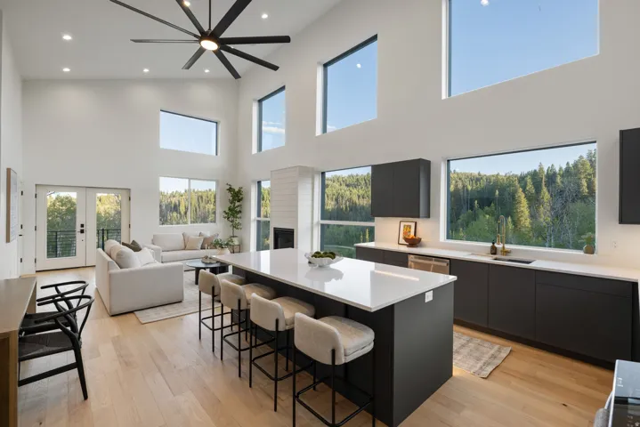 Vaulted ceiling with a large ceiling fan, recessed lighting, wood-finish flooring, a kitchen island with a light-toned countertop, and a fireplace with a white shiplap-style surround
